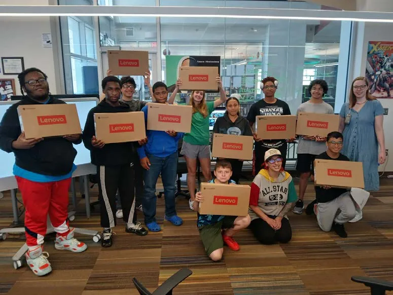 Young participants and staff holding up boxes with their new laptops